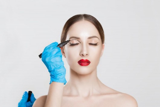 A doctor makes marks on the eyelid of a beautiful girl before cosmetic procedure