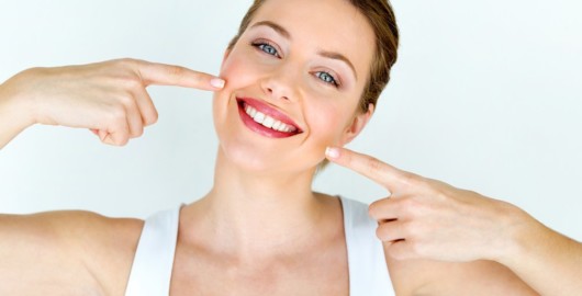 A beautiful girl on white background is smiling and pointing to her mouth and perfect white dental implants